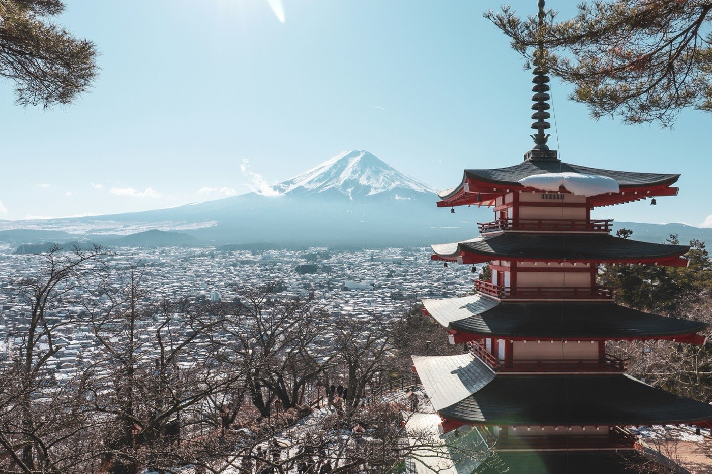 Une pagode rouge à cinq étages sur une colline enneigée, le mont Fuji au loin derrière la ville