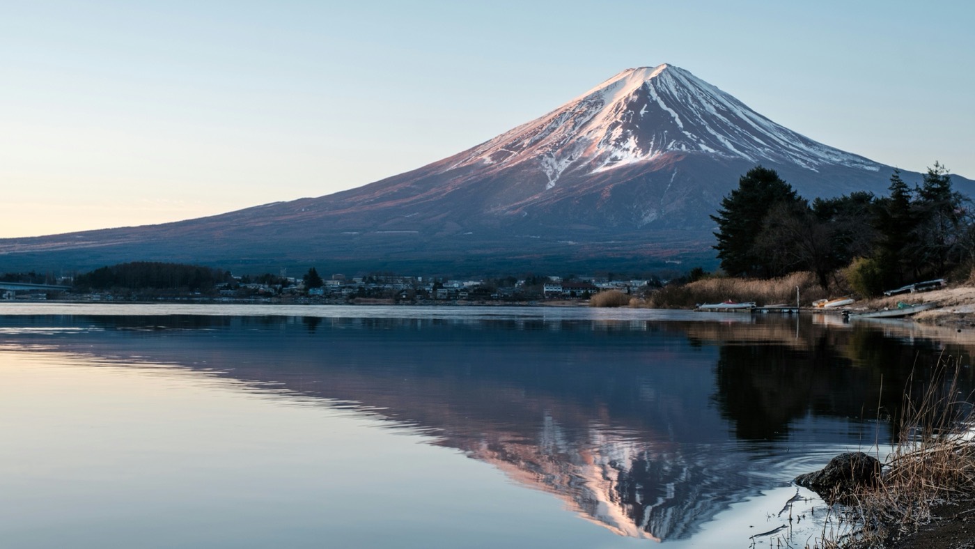 Le mont Fuji enneigé au lever du jour, reflété dans un lac bordé d'une petite ville