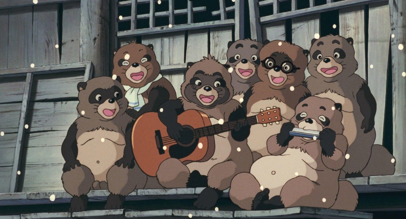 Sept tanuki assis sous la neige devant une maison de bois, l'un joue de la guitare, un autre de l'harmonica, les autres chantent