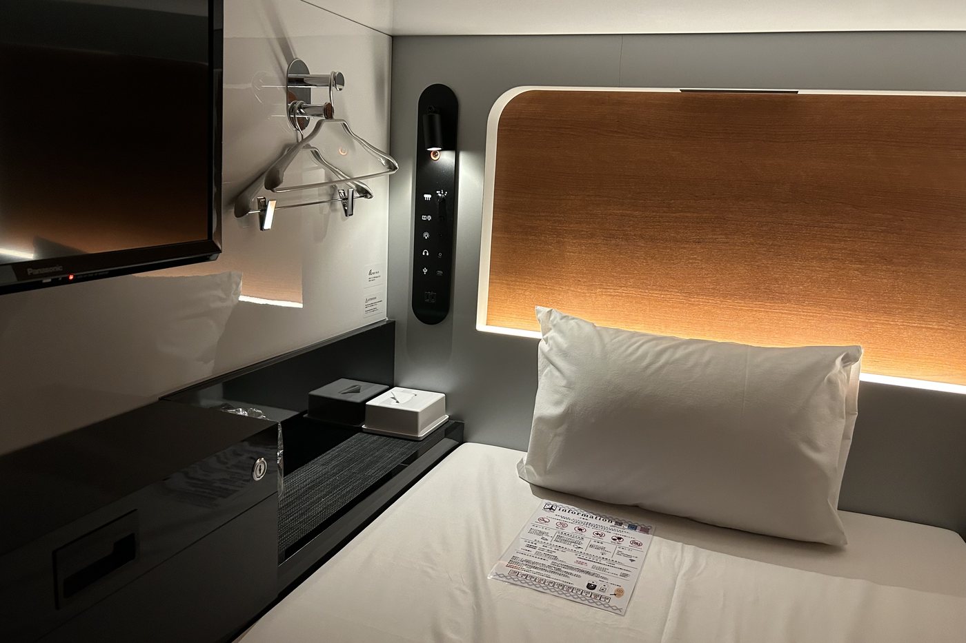 Inside a First Cabin berth: bed, television and a backlit wooden headboard.