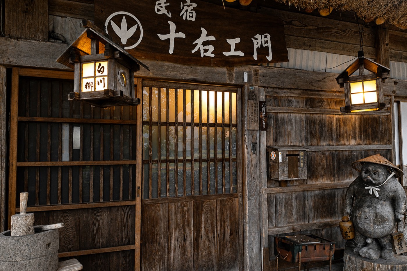 The entrance to a minshuku in Shirakawa-go, wooden sign and lit lanterns.