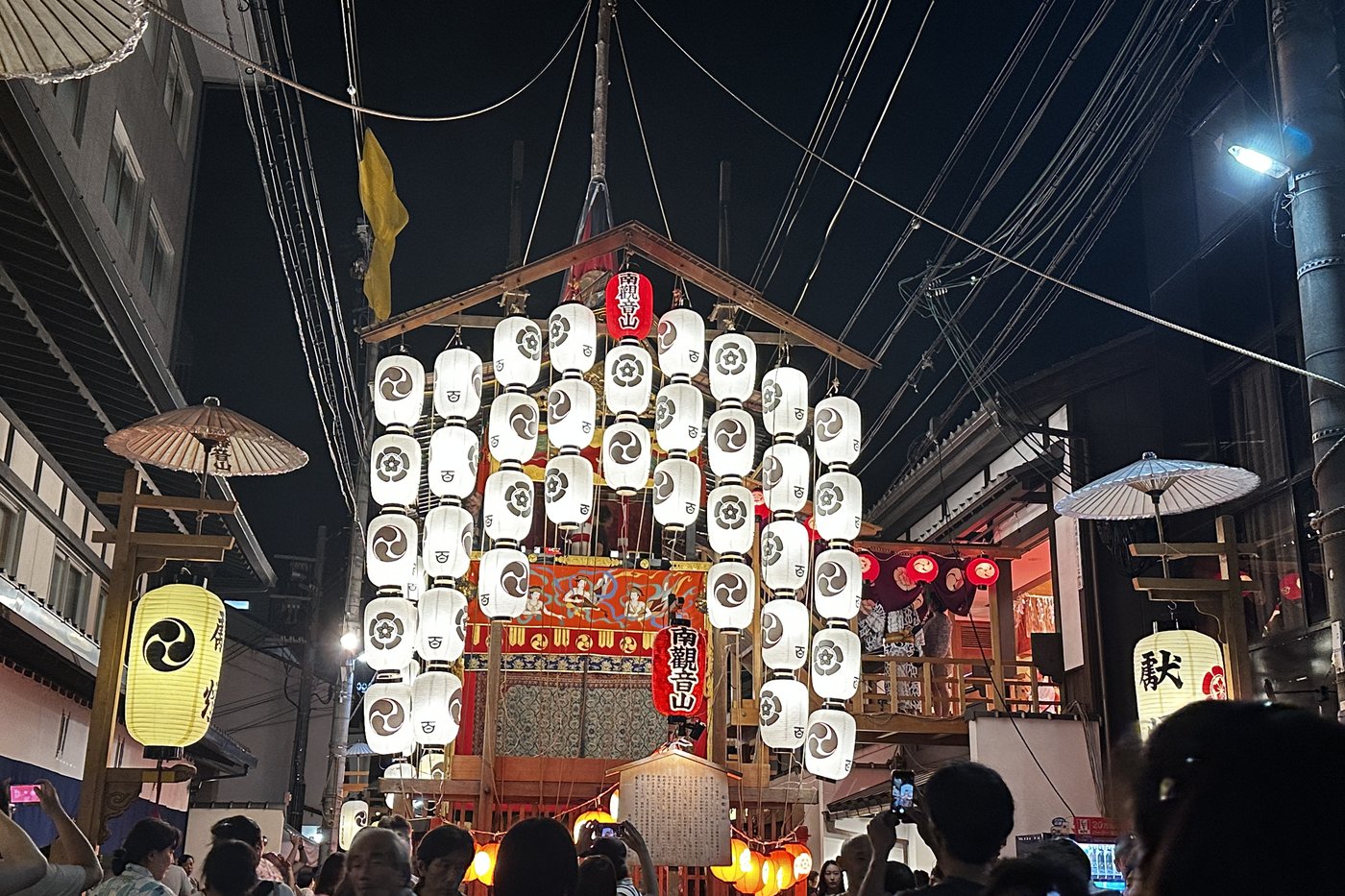 Char Niwatoriboko du Gion Matsuri illuminé de lanternes blanches la nuit, foule sous le char à Kyoto.