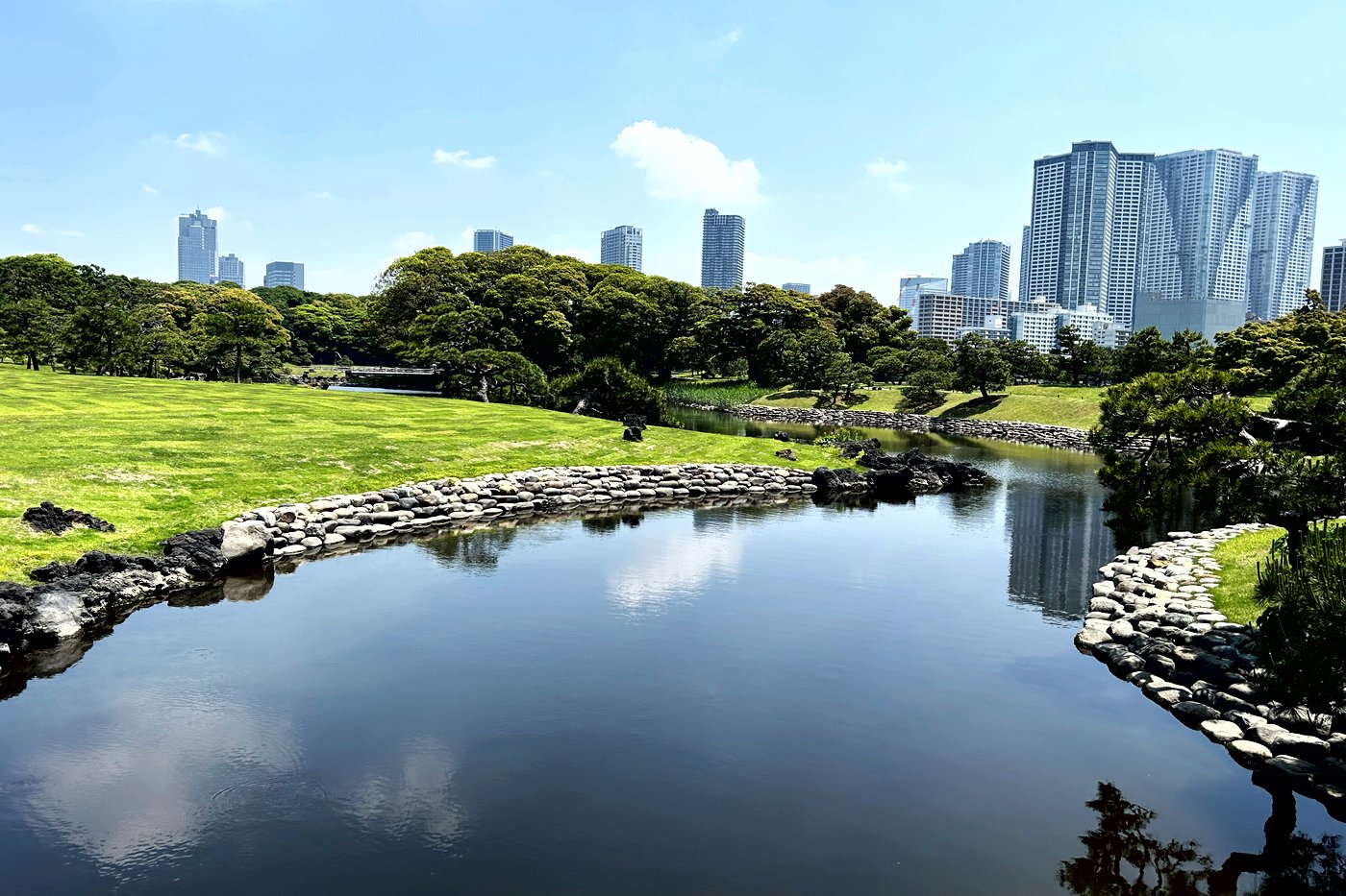 Étang du jardin Hama-rikyu à Tokyo, bordé de pierres, gratte-ciel de Shiodome en arrière-plan.