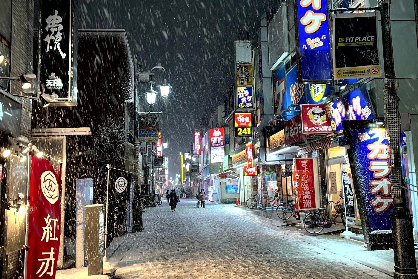 Rue commerçante de Crea Mall à Kawagoe sous la neige la nuit, néons de karaoké et lanternes allumées.