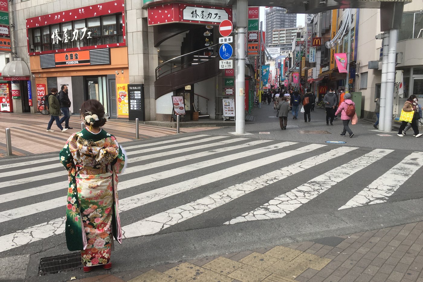 Jeune femme de dos en furisode vert et or, à un passage piéton de Tokorozawa pour la Journée de la majorité.