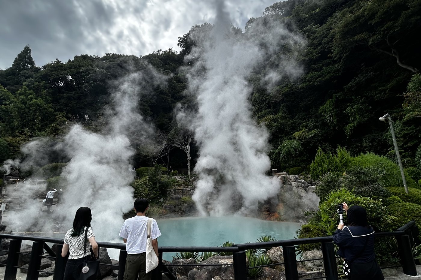 Bassin thermal bleu turquoise fumant de l'enfer de Umi Jigoku, visiteurs de dos au premier plan, à Beppu.