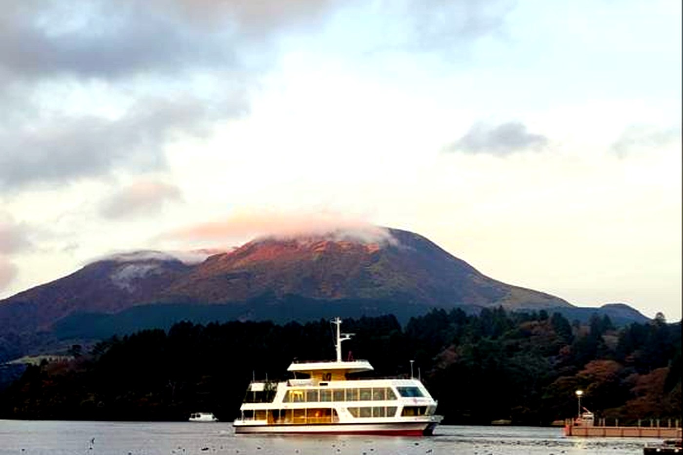 A cruise boat on Lake Ashi at dusk, a cloud-covered summit behind it.
