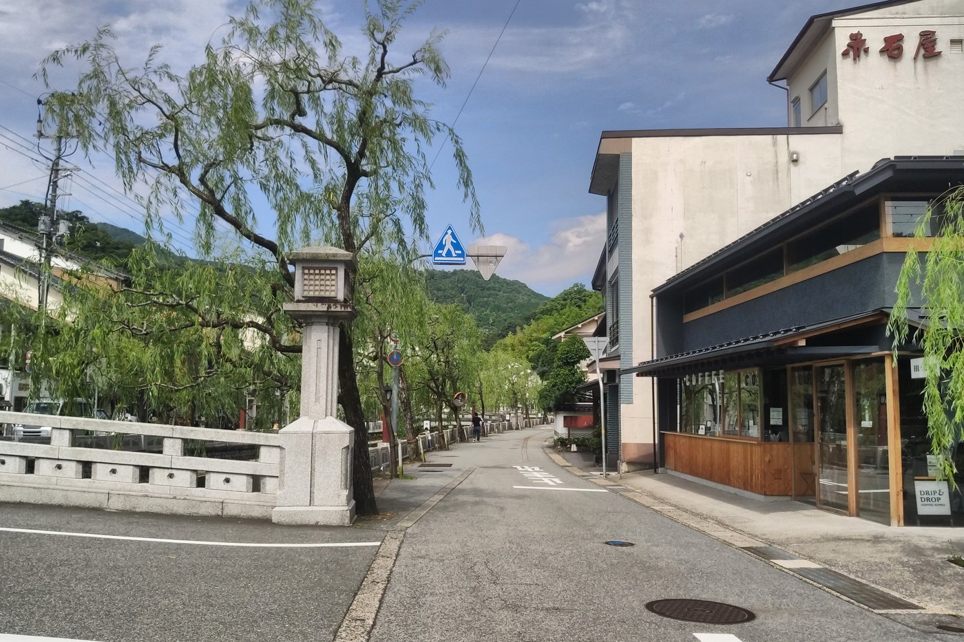 A street of willows and shops along the Kinosaki Onsen canal, mountains behind.