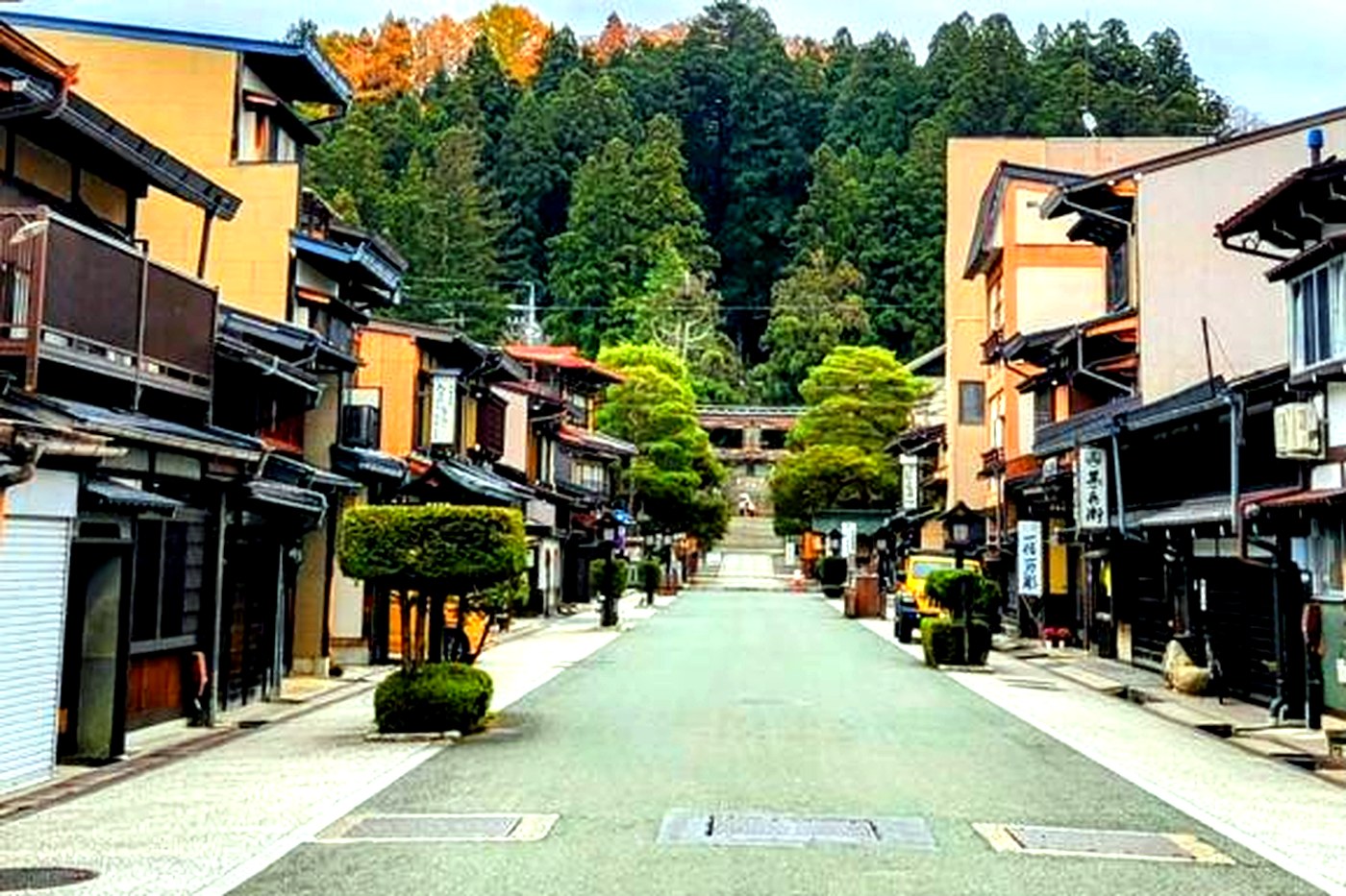 The historic San-machi Suji street in Takayama, wooden houses and traditional shops, a wooded hill behind.